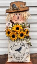 Load image into Gallery viewer, Decorative scarecrow with sunflowers and a seed bag on a wooden surface.